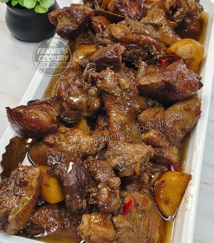 A plate of Chicken and Pork Adobo garnished with herbs and served with rice