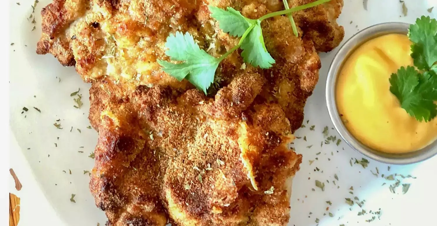 Crispy air fryer chicken thigh schnitzel served with lemon wedges and garnish.