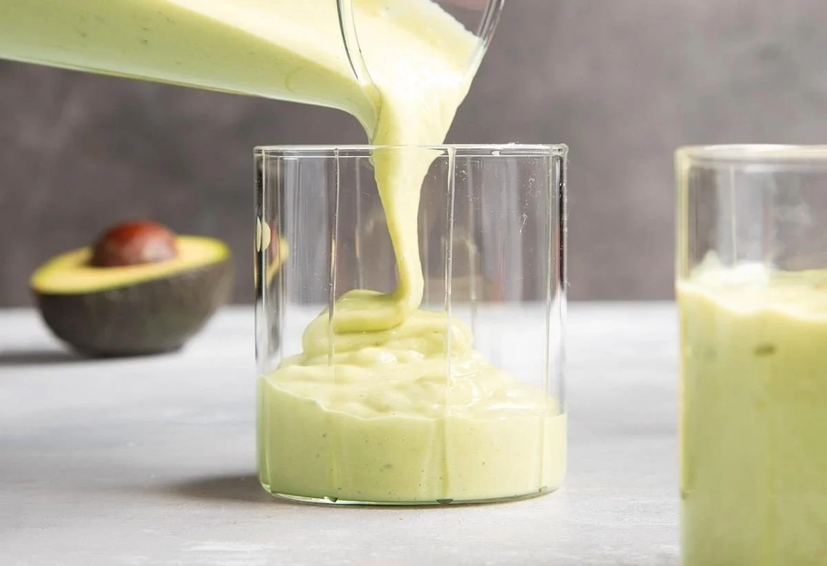 Creamy avocado banana smoothie in a glass with fresh ingredients.