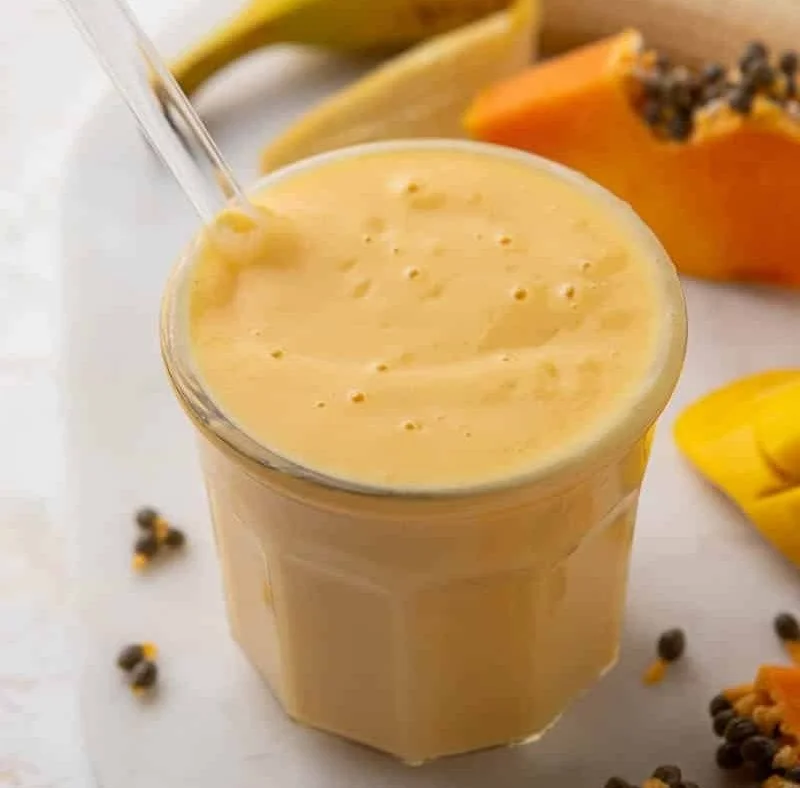 Creamy mango papaya smoothie in a glass with fresh fruit on the side