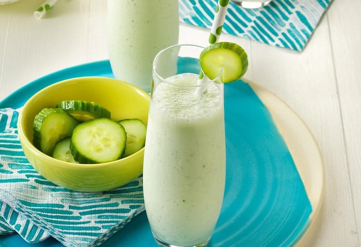 Cucumber-melon smoothies in a glass with fresh ingredients on a wooden table