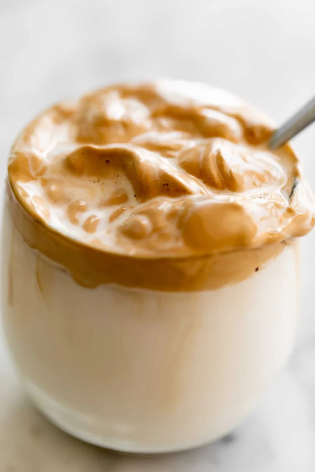 A cup of Dalgona Coffee topped with whipped froth and served on a wooden table