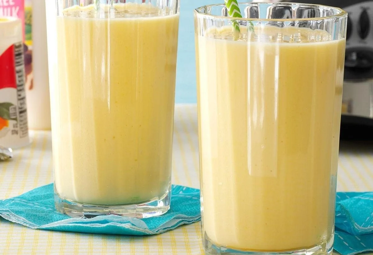 Delicious mango peach smoothies in a glass with fresh fruit around.