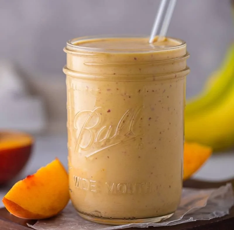 No sugar added banana peach smoothie in a glass with fresh fruit garnish