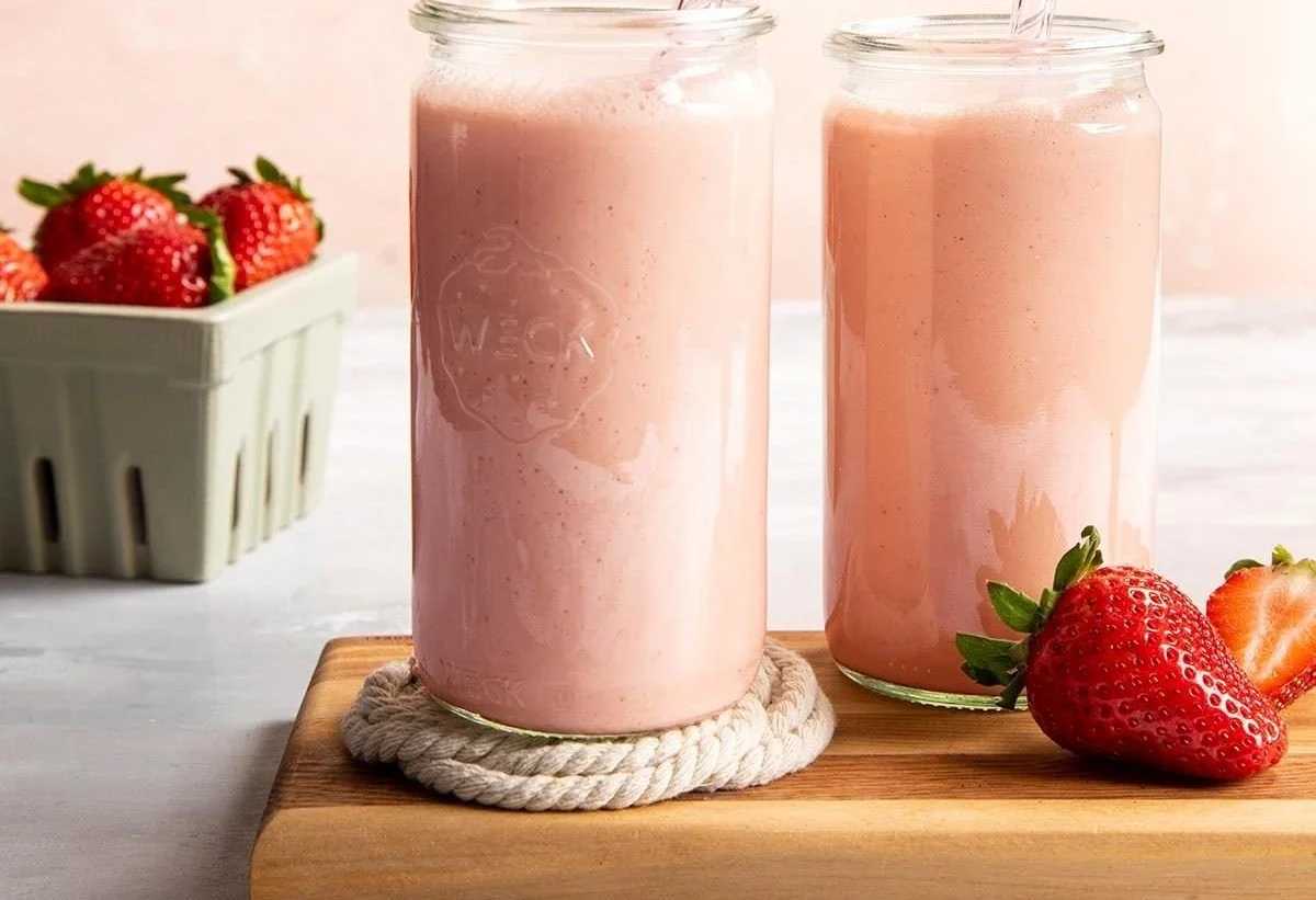 Delicious strawberry smoothie in a glass with fresh strawberries on the side.