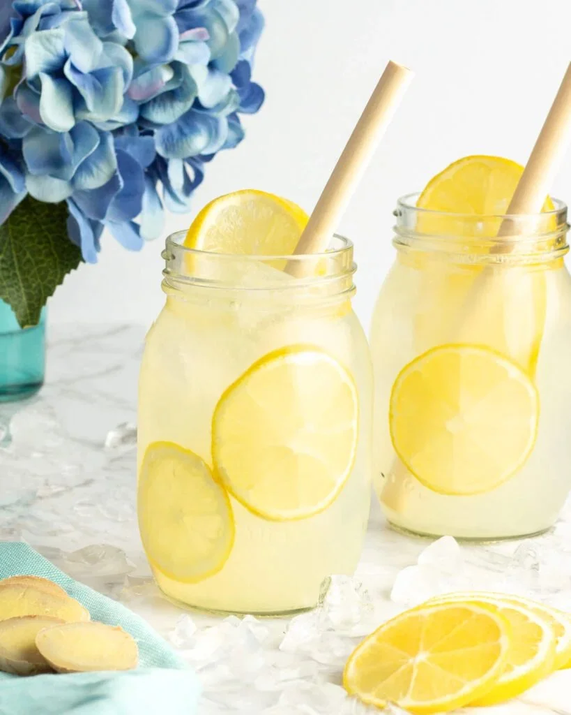 A refreshing glass of ginger lemonade with lemon slices and fresh ginger on a table.